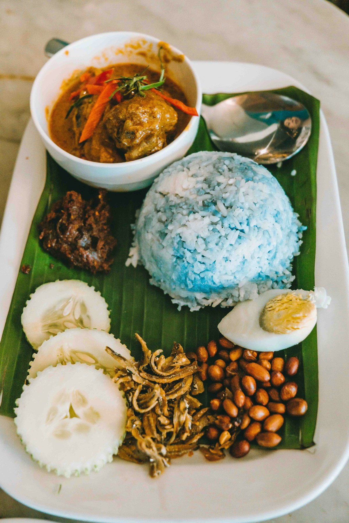 Nasi lemak with blue butterfly pea rice, curry, sambal, anchovies and peanuts on banana leaf, Kuala Lumpur, Malaysia