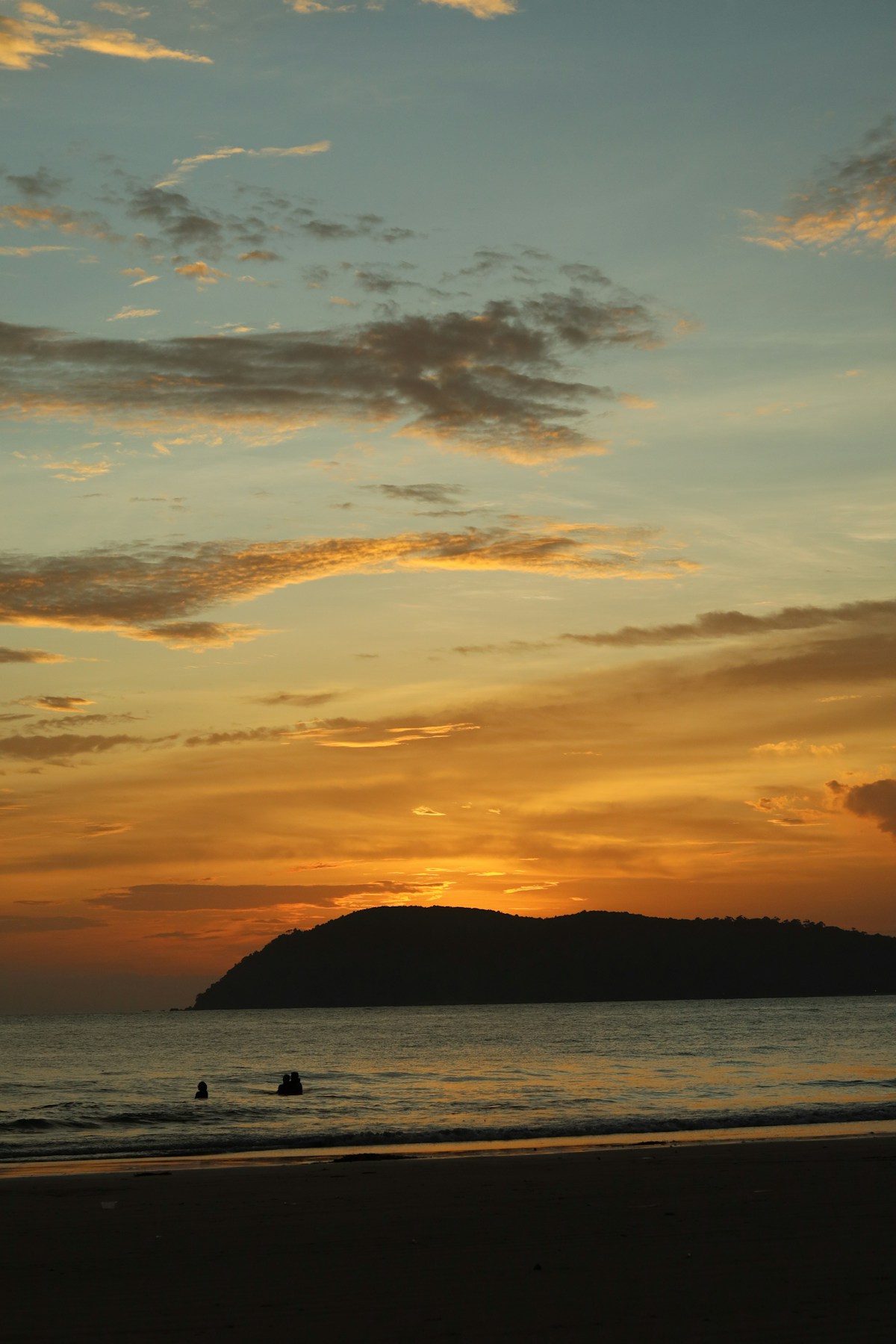 Couple silhouetted on Pantai Tengah beach at sunset, Langkawi, Malaysia