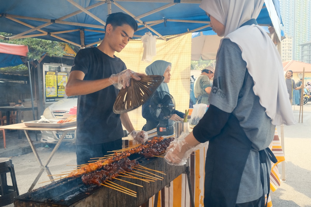 Street vendor grilling satay skewers at an outdoor market stall in Penang, Malaysia