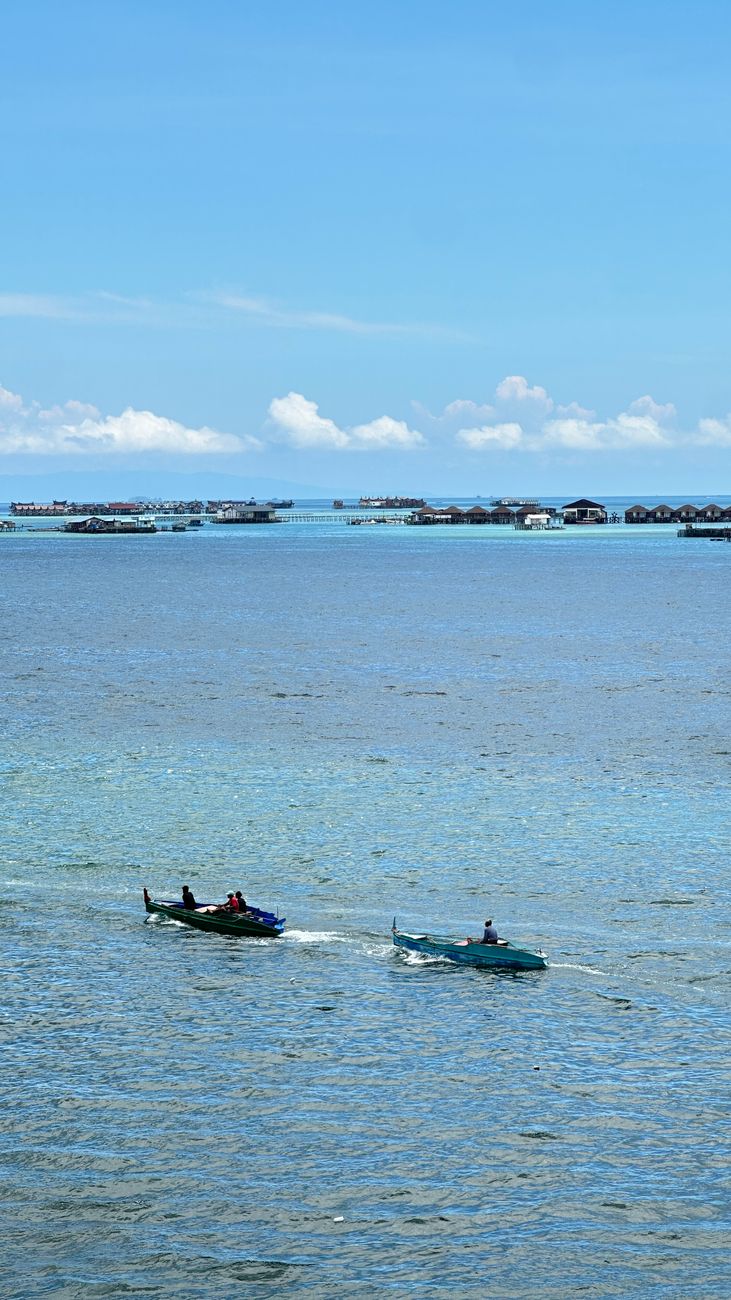Two fishing boats crossing turquoise water near Semporna with Mabul Island stilt resort visible in background, Sabah, Malaysia
