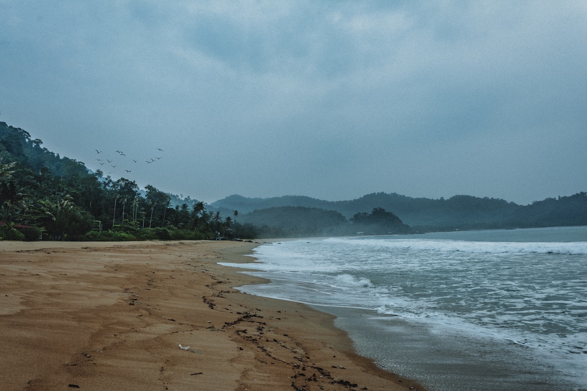 Sandy beach with jungle-covered hills and waves, Tioman Island, Pahang, Malaysia
